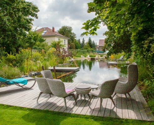 Blick auf einen Schwimmteich und eine Holzterrasse mit einer Sitzgruppe