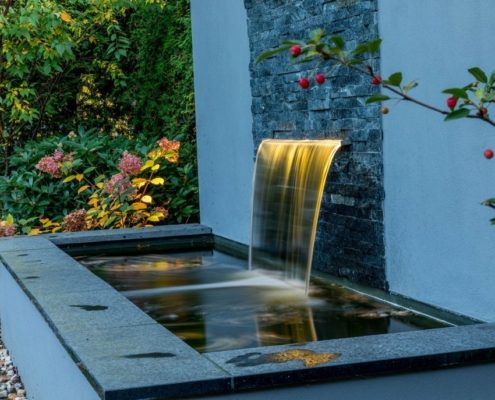 Wasserfall im Hausgarten beleuchtet am Abend