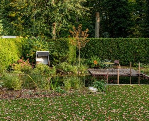 herbstlicher Schwimmteich mit einer Holzterrasse in einem Hausgarten