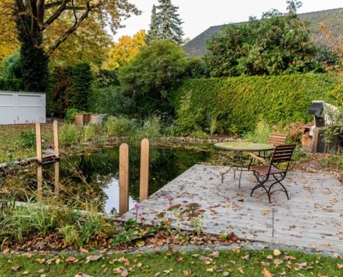 Holzterrasse mit einer Sitzgruppe am Schwimmteich im Herbst