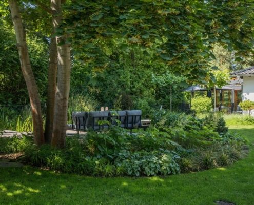 Eine Sitzgruppe neben dem Schwimmteich Sitzgruppe im Garten umgeben von Stauden. EIn Haus neben der Sitzgruppe