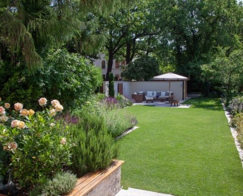 ein mediterraner Stadtgarten mit viel Pflanzen Rasenfläche mit einer Loungeecke und einem Kräuterbeet